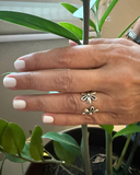 Hand wearing a daisy silver ring with a plant in the background