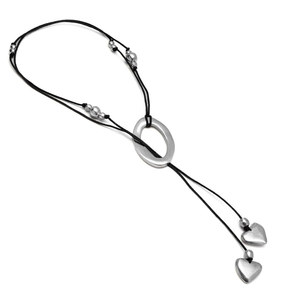 A silver-toned lariat necklace featuring a large oval center pendant, small silver beads on black cords, and two dangling heart charms at the ends, shown on a plain white background.