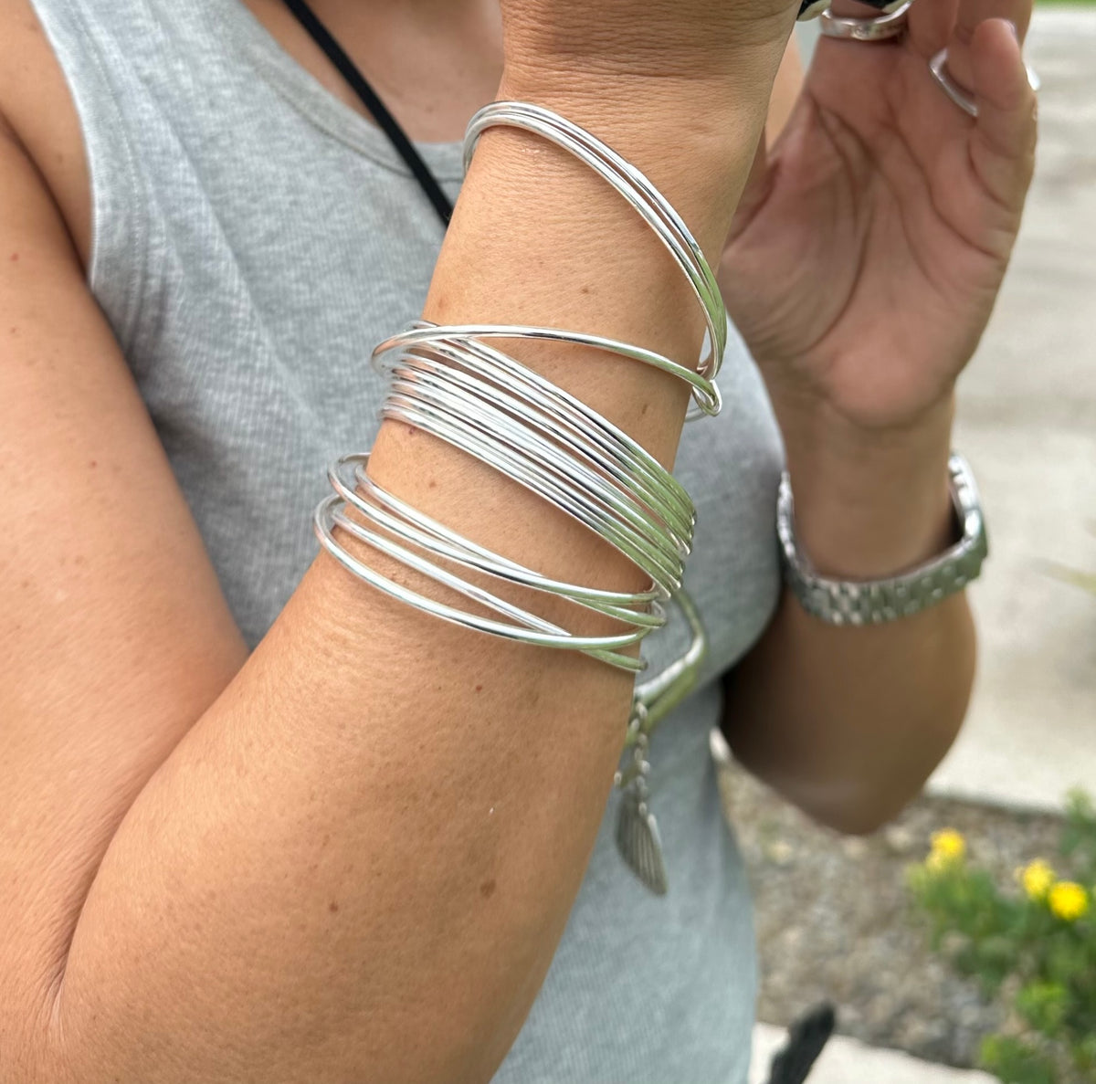 Person wearing multiple silver bracelets on their wrist with a blurred background