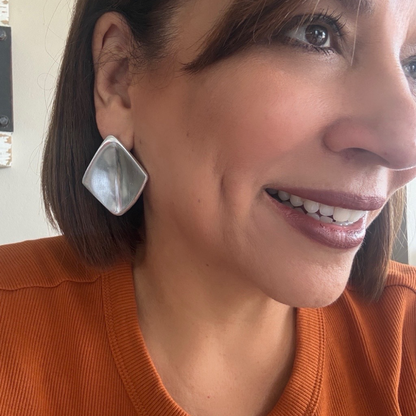 Vestopazzo Rhombus Stud Earrings – Smiling woman wearing oversized silver rhombus stud earrings with orange top | Místika Style