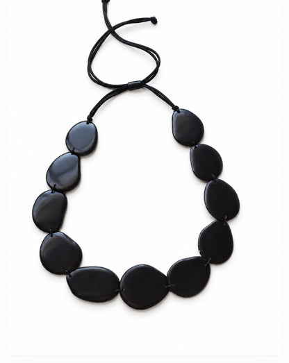 A black beaded necklace made of smooth, irregular teardrop-shaped Tagua beads on a black adjustable cord, displayed on a clean white background.