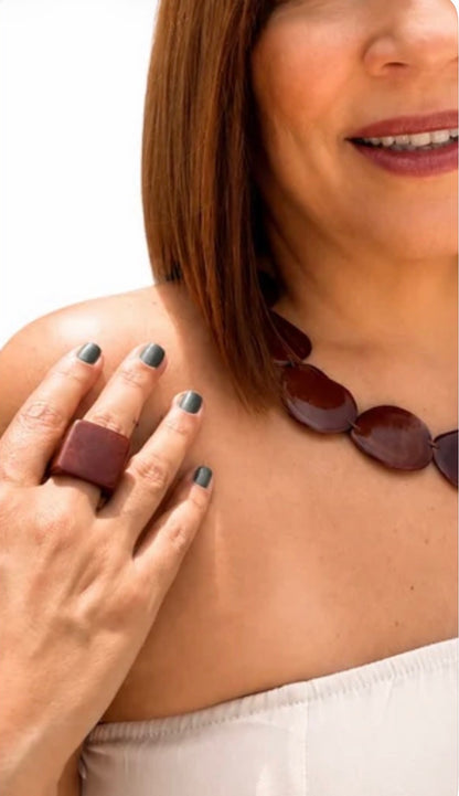Model wearing a brown statement necklace with glossy, rounded organic-shaped Tagua pieces resting along the collarbone