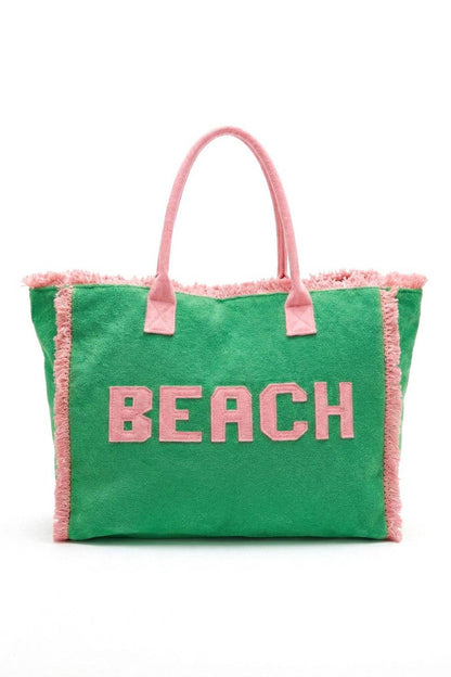 Green beach bag with pink handles and 'BEACH' text on a white background