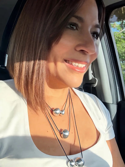 Vestopazzo Three Layers Necklace – Smiling woman wearing triple-strand silver sphere necklace in sunlight with white top | Místika Style

